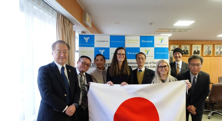  Jun Nishida, Dr Masamoto Tafu, Kato Takaaki, Natasha Lloyd, Dr Yoshiaki Kunieda, Charlotte Buick, Dr Shoichi Furuyama, Dr. Yasumasa Minemoto at Toyama College, National Institute Of Technology with a Japanese flag.